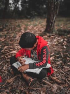 A young boy engrossed in reading a book while sitting on the forest ground in Tuaran, Sabah, Malaysia.