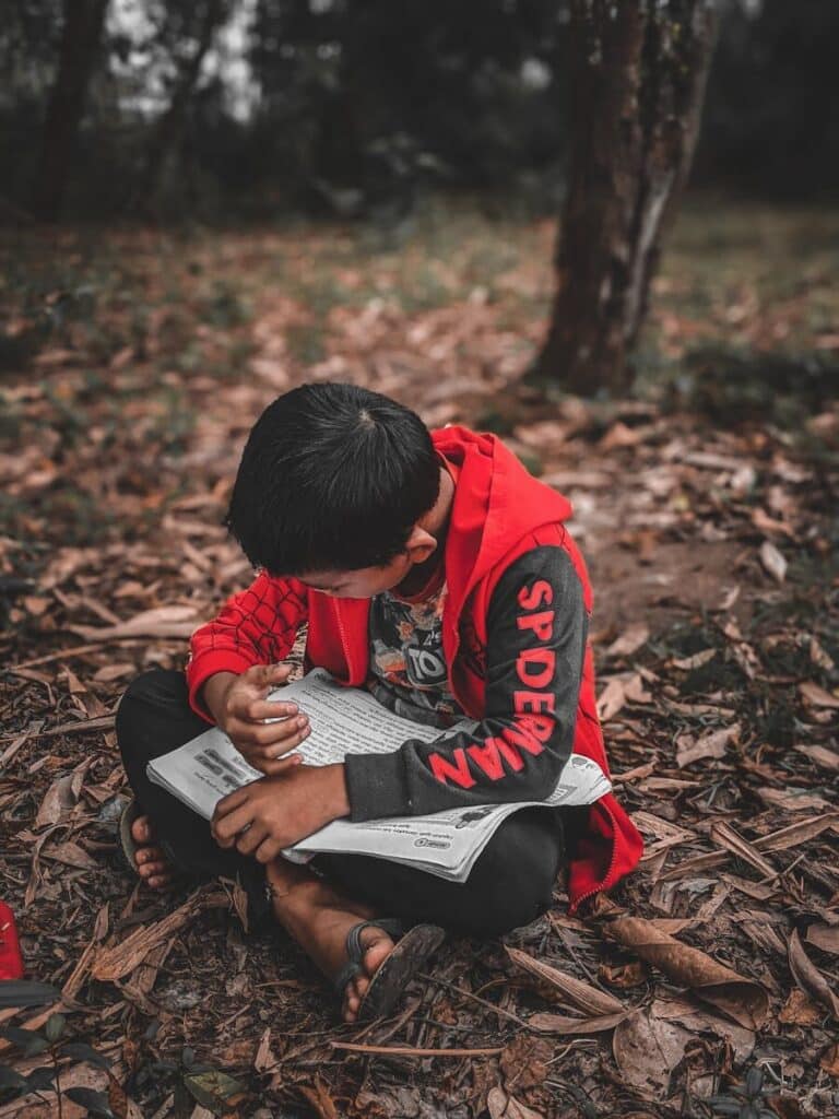 A young boy engrossed in reading a book while sitting on the forest ground in Tuaran, Sabah, Malaysia.